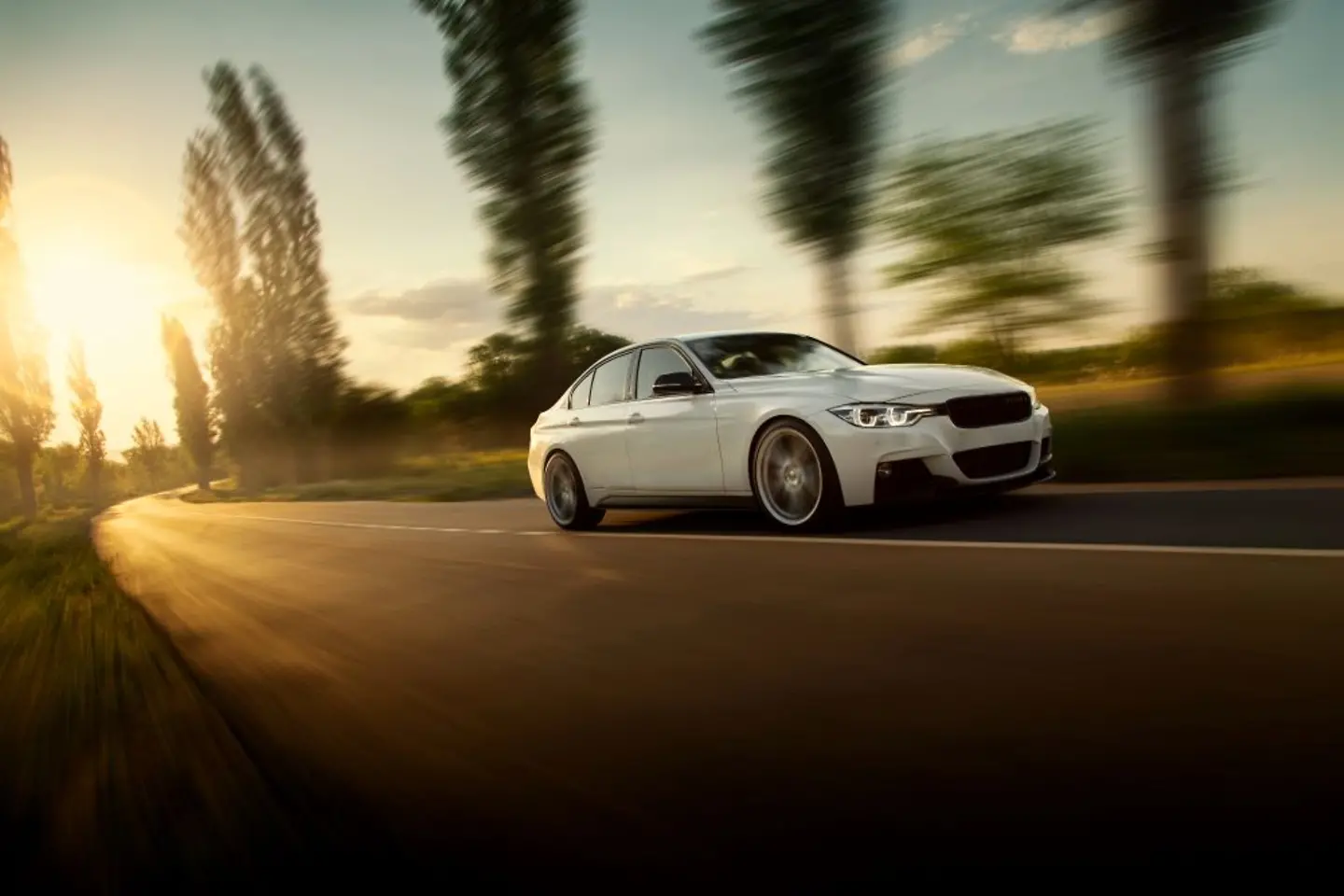 Weißes Auto fährt auf einer Landstraße im Sonnenuntergang