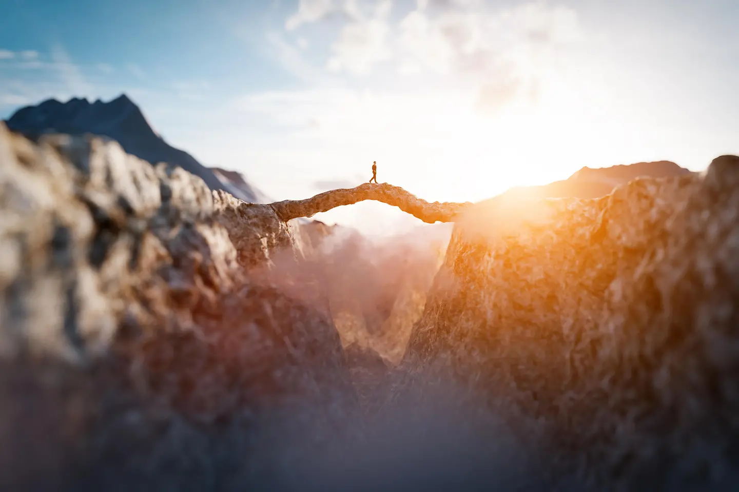 Hombre caminando hacia el sol sobre un impresionante puente de montaña