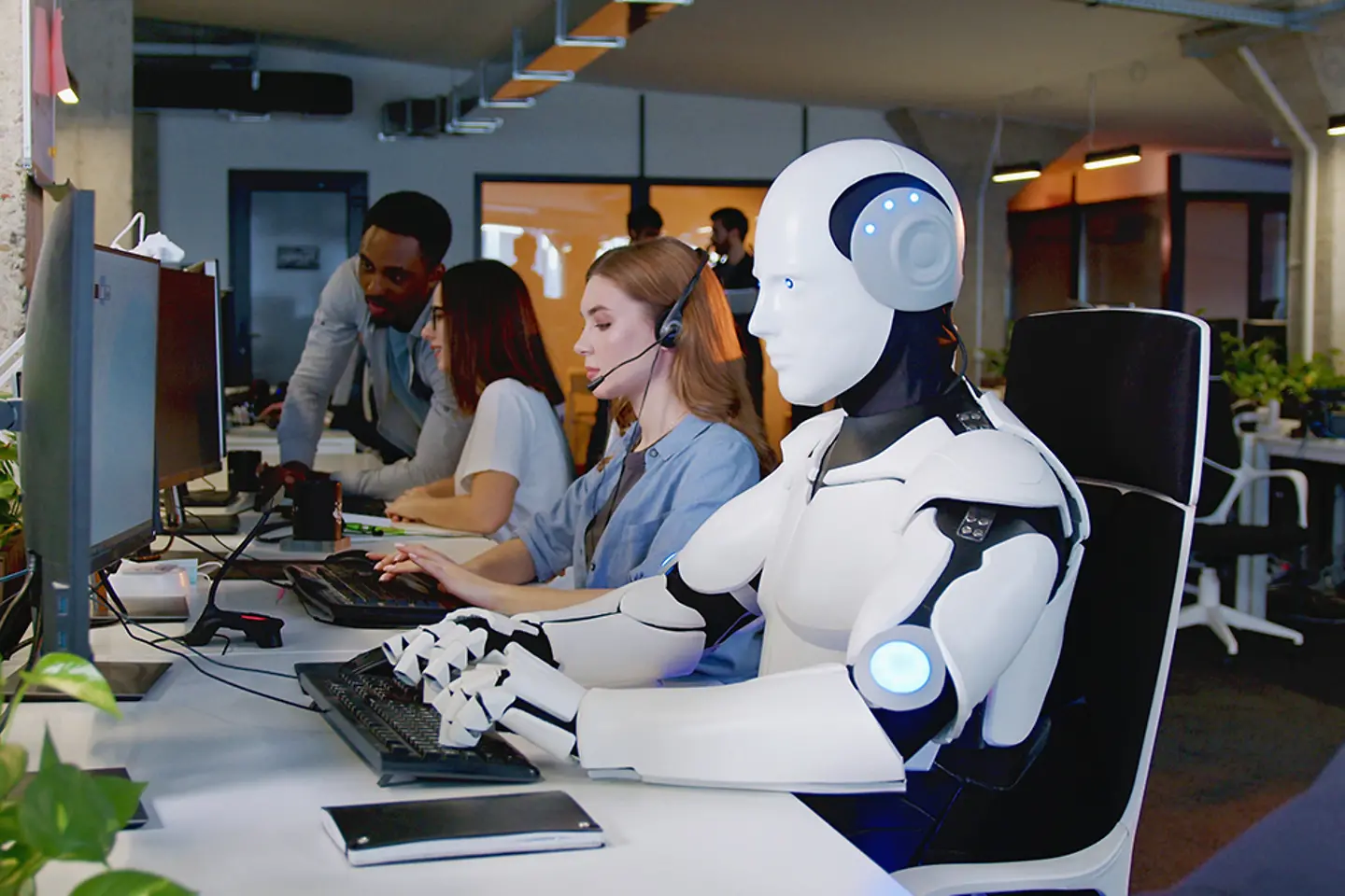 Roboter arbeitet in einem Büro neben menschlichen Mitarbeitern an einem Computer